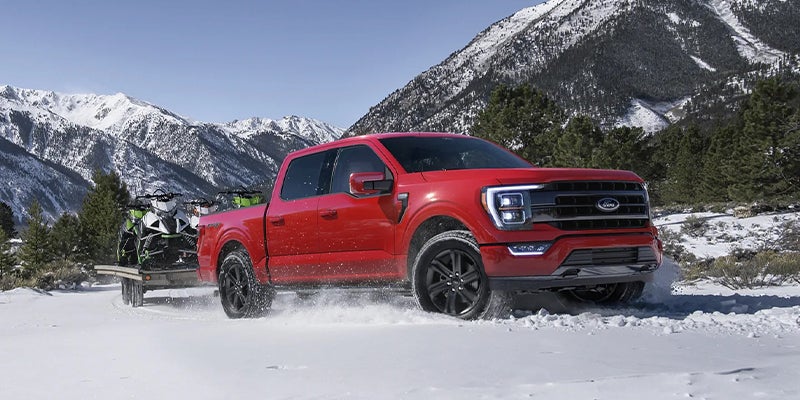 A red Ford F-150 hauls a snowmobile trailer through the snow.