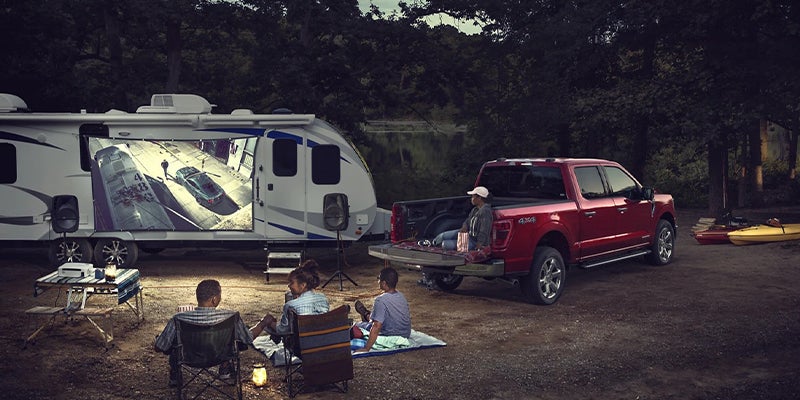 A Family watches a movie being projected on the side of their camper, that is hooked up to their Ford F-150