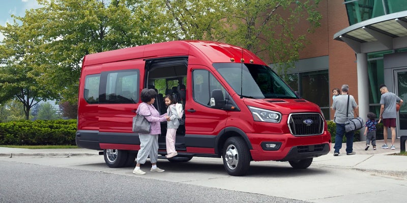 A mother helps her child our of a red Ford Transit Van