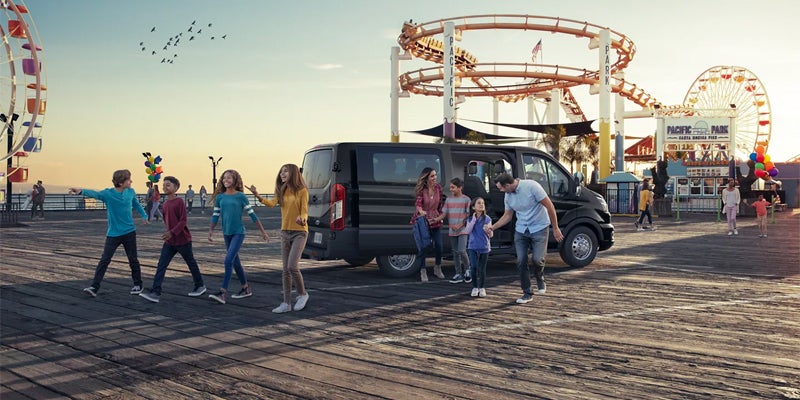 A family climbs out of a Ford Transit van , onto an amusement park boardwalk.
